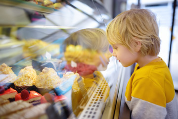 Little boy is admiring cakes and other sweets on the showcase in cafe or supermarket