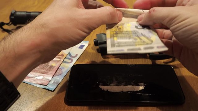 Rolling a bill to snort cocaine. Table full of drugs and weapons.