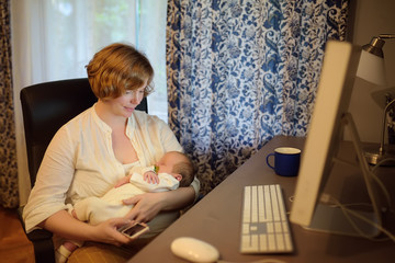Fototapeta na wymiar Young mother holding baby, chating by smartphone and working pc at home. Motherhood, business, housework.