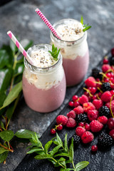 2 jars of milkshake or smoothie with cranberries, strawberries and blueberries standing on stone backdrop.