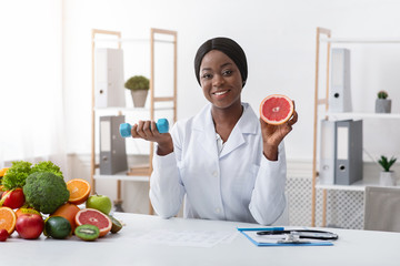 Smiling nutritionist holding grapefruit and barbell in her hands