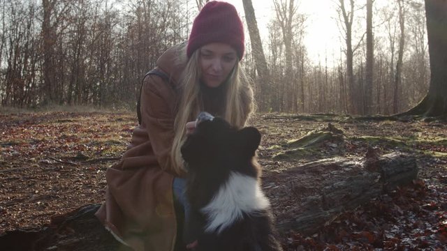 Pretty girl feeding her dog with goodie snack after training in forest in autumn