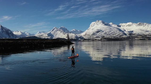 Following drone shot of a paddle boarder traveling towards a magnificent mountain range.