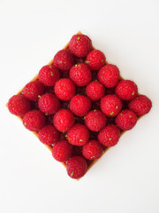 French dessert. Tart with raspberries. Almond frangipane and raspberry coulis inside of a tart. Decorated with fresh raspberries and lime zest. White background. Top view.