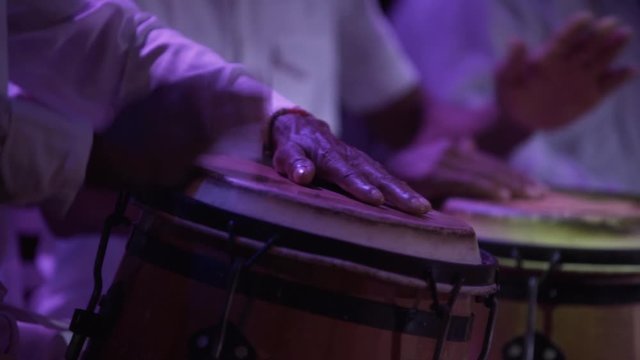 close up slow motion of musician hands playing bongos , performance lifestyle , afro drums men with white traditional costumes