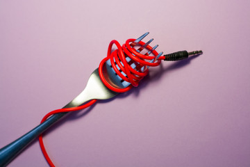 Pink background. Red, pink, yellow headphone cable is wound on silver fork. Spaghetti.