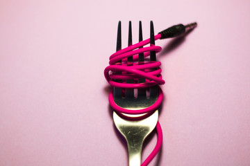 Pink background. Red, pink, yellow headphone cable is wound on silver fork. Spaghetti.