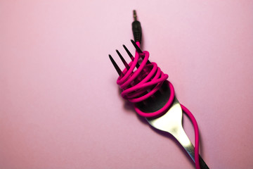 Pink background. Red, pink, yellow headphone cable is wound on silver fork. Spaghetti.