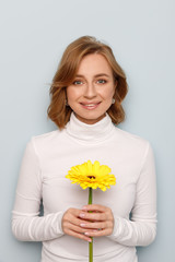 Pretty joyful woman holding single beautiful gerbera flower, smiling,  on blue background.  Spring...