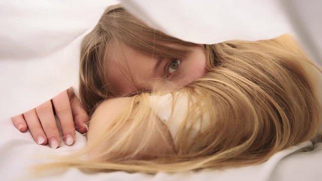 Close up of Caucasian blonde woman wakes up inside a white blanket