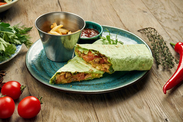 Appetizing shawarma roll with meat, salad and homemade sauce in thin pita bread in blue plate isolated in grey background. Eastern cuisine. Sliced kebab with grilled meat.