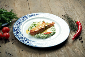 Delicious grilled salmon steak filet with peas in a creamy sauce in a white plate on a wooden background. Tasty seafood