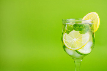 Refreshing detox drink of lemon, mint, cucumber, with ice in a transparent glass. Green background. Copy space