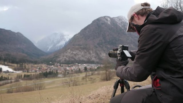 Photographer setting up a camera to capture photos during a storm in Slovenia. Looking over a village Mojstrana in Slovenia with the Julian Alps covered in Snow. Triglav National Park.