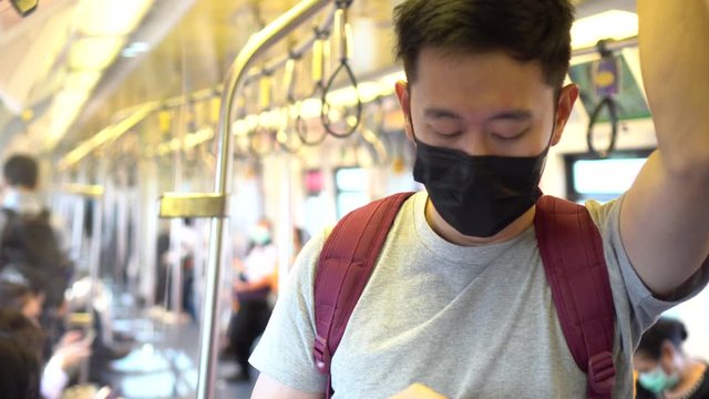 Close up of one young Asian man wearing a black surgical face mask and using mobile phone in subway train during new type Coronavirus Covid-19 pneumonia outbreak and pm 2.5 smog air pollution crisis