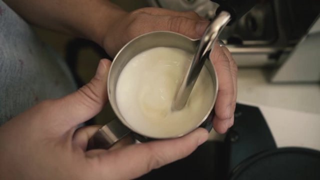 Barista holding a jug of foam texturing milk with the machine vaporizer, view from the top
