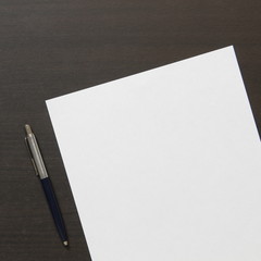 Template of white paper with pen on dark wenge color wooden background.