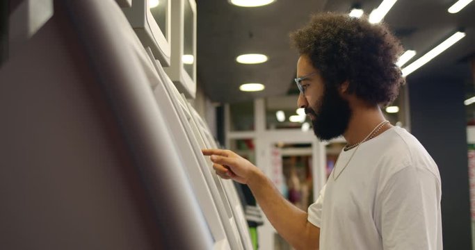 Side view of bearded man using cashmashine and taking money. Guy in 30s pressing on display while standing near self service terminal. Indoors. Concept of people and technology.