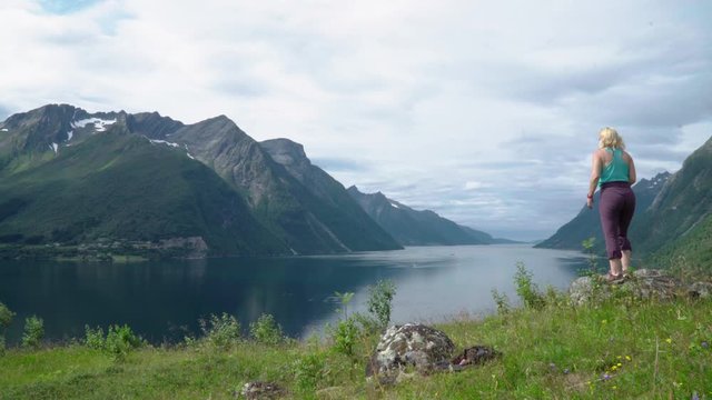 Woman walking to viewpoint before taking a panoramic picture of a beautiful norwegian fjord