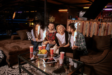 Fototapeta na wymiar Multi races group of young on sofa holding sparkling fireworks campfire on night party