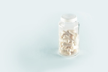 Glass bottle with capsules on white background. White capsules in vial. Healthcare and medicine