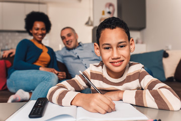 Parents helping their son with his homework at home in living room.
