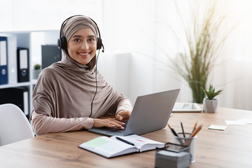 Arab female call center operator in hijab and headset at workplace