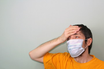 Middle-aged adult man in a yellow T-shirt on a gray background in a medical mask holds his hand...