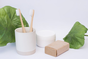 Two eco bamboo zero waste toothbrushes in a glass with organic cosmetics on a white background