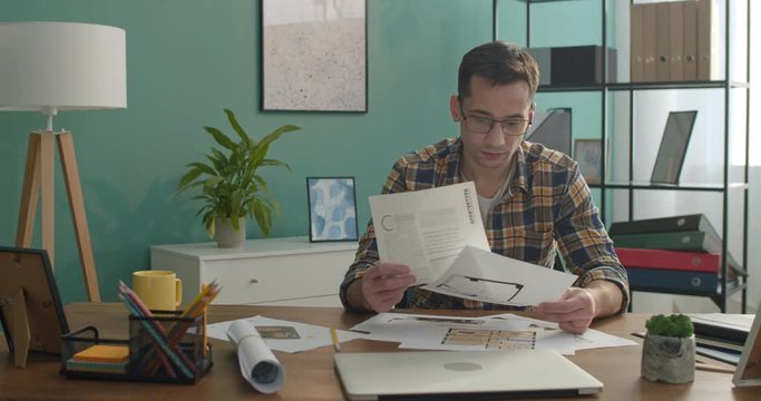 Caucasian man architect or designer in glasses looking at drafts, graphics, drawings and plans at the working table.