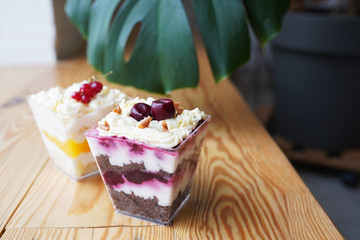 Desserts blueberries with cream and chocolate biscuit and peach with cream and vanilla biscuit decorated berries in square glasses on wooden table.