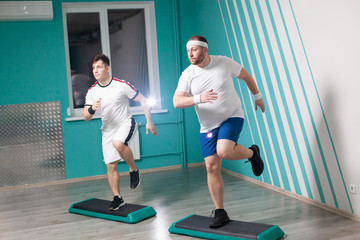 Fat man is very hardworking doing step-up exercises on steps during group fitness classes. Excess weight