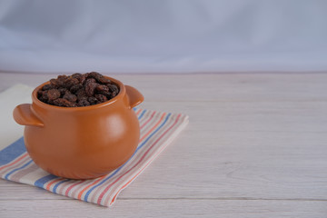 A small brown pot filled with raisins on a light countertop and a striped towel.