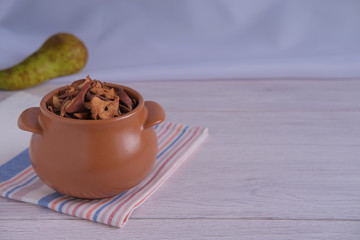 A small brown pot filled with dried pears (dried fruit) on a light countertop and a striped towel. A pear is shown in the background, light toning is used.