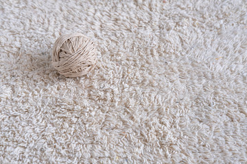 A ball of thick thread lies on a light beige fleecy carpet.