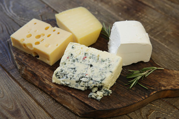 various types of cheese maasdam and parmesan and blue cheese captured and feta on a wooden board. Organic farm dairy products.