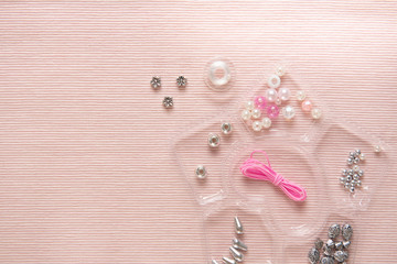 background of pink fabric with accessories for weaving with beads with a container for beads