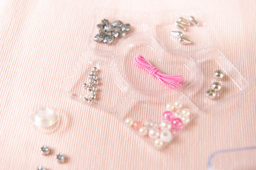 background of pink fabric with accessories for weaving with beads with a container for beads