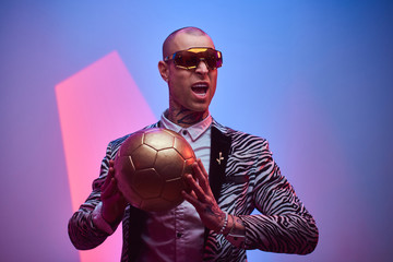 Fashionable, handsome, tattooed, bald male model posing in a studio for the photoshoot wearing fashionable custom made zebra striped style tuxedo, glasses and rose patterned shirt, holding a golden