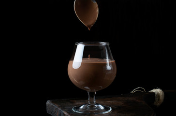 Chocolate pudding is dripping from the spoon into a glass against the black background