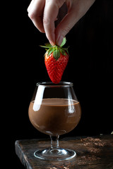 Strawberry dipped into chocolate sauce in a glass against the black background