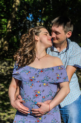 Young couple in love on a walk in the park, husband hugs pregnant wife by the belly, happy family