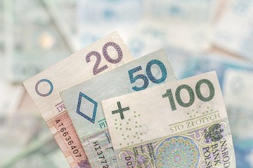 Banknoty o nominałach 20, 50 i 100 zł leżą na pierwszym planie. W tle banknoty o różnych...