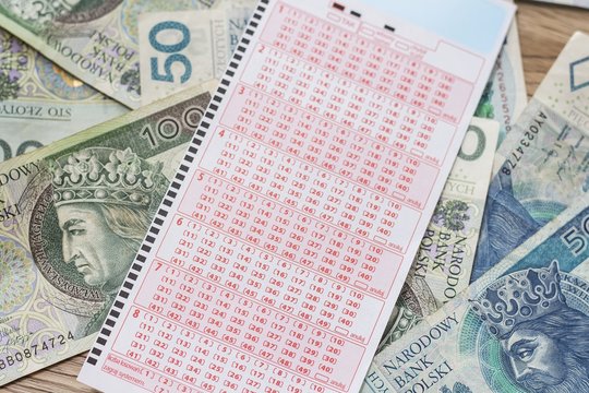 Kupon lotto leży na banknotach PLN.