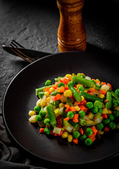 Mixed vegetables on a black plate on Dark grey black slate background