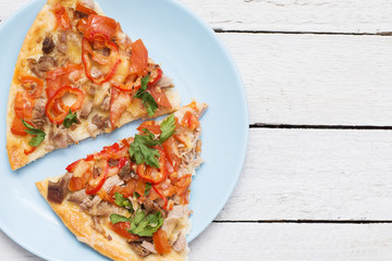 Overhead view of two freshly baked slices of pizza with cheese, tomato, olives and herbs on a blue plate over a white wooden background