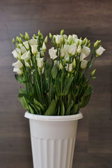 Beautiful lush bouquet of white flowers on the wooden background. Stylish floristic composition in the long vertical vase. Spring time and holidays concept, interiors decorating