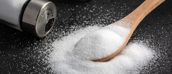 White sea salt for cooking food in Small glass bottles and wooden spoons on a stone tray background.
