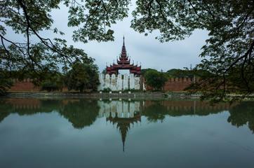 Fototapeta premium Mandalay Palace wall and moat under grey sky, Myanmar. Photo with foliage frame
