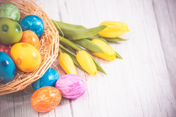 Obraz na płótnie Canvas Beautiful group Easter eggs in the spring of easter day, red eggs, blue, purple and yellow in Wooden basket with tulips on the wood table background